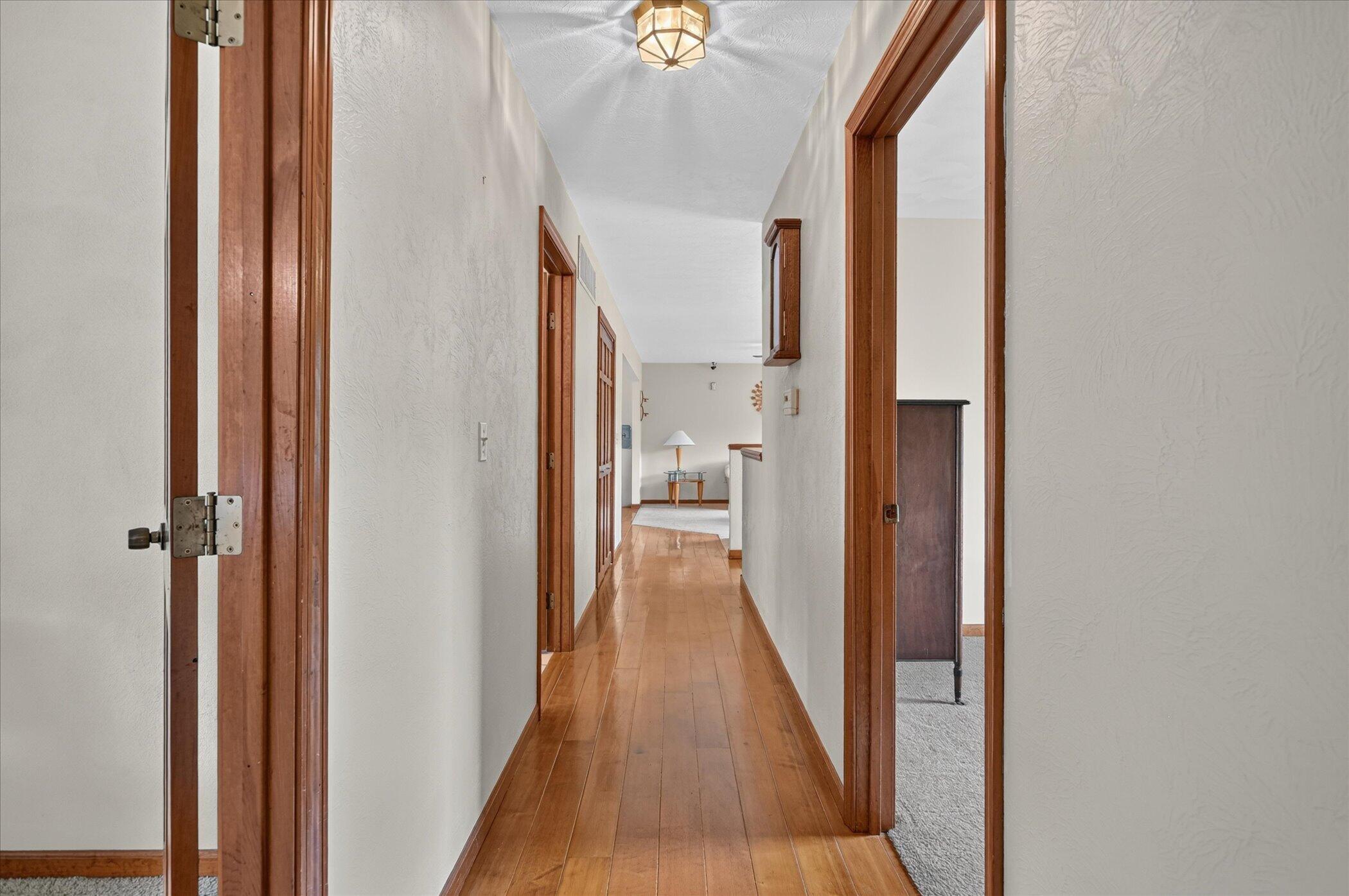Long hallway with hardwood floors, wood trim, and a small table and lamp at the far end.