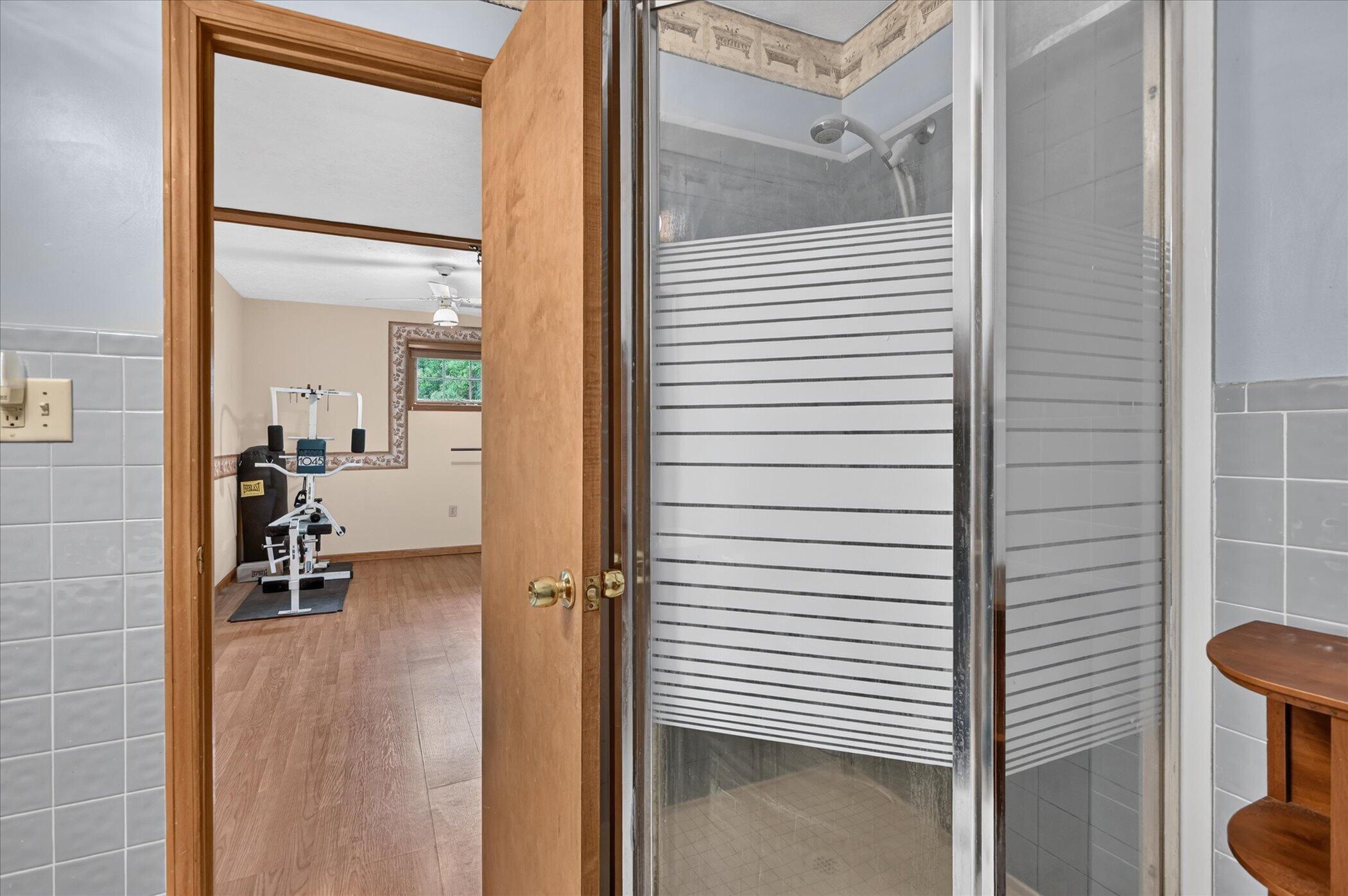 Bathroom shower with striped frosted glass beside a doorway to a room with exercise equipment.