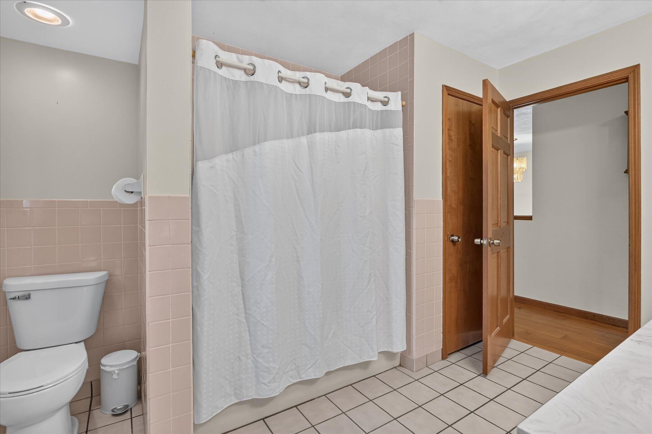 Bathroom with a white shower curtain, pink tile, toilet, and open wooden door.
