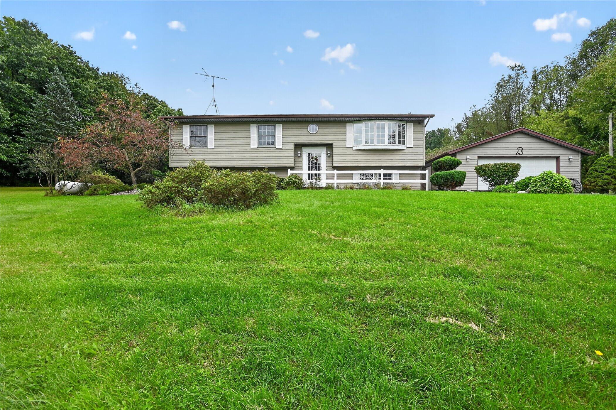 Split-level home with bay window and garage beyond a broad green lawn.