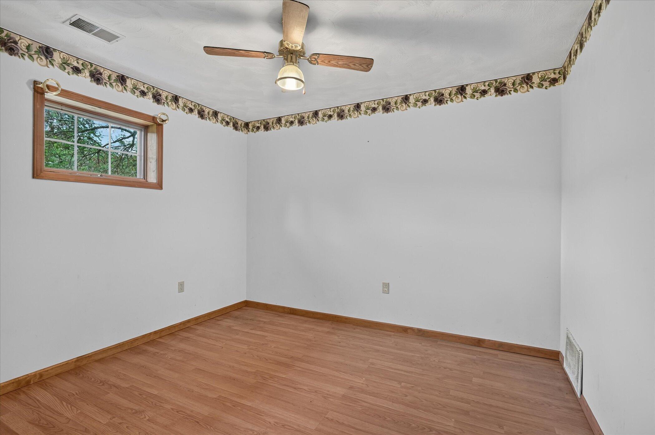 Vacant room with wood-look flooring, a small window, and a ceiling fan with light.