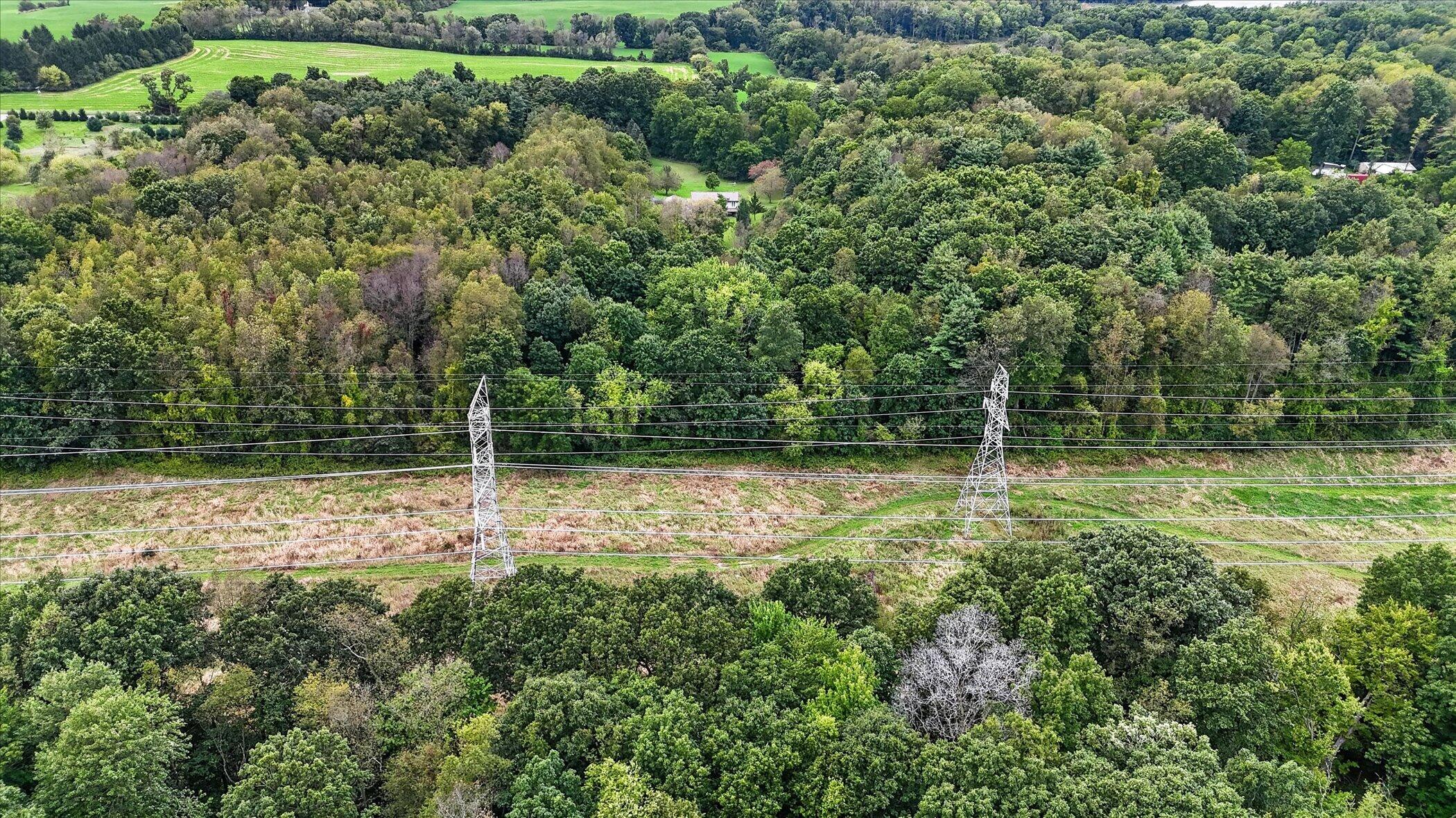 Aerial view of wooded property crossed by a power-line corridor and transmission towers.