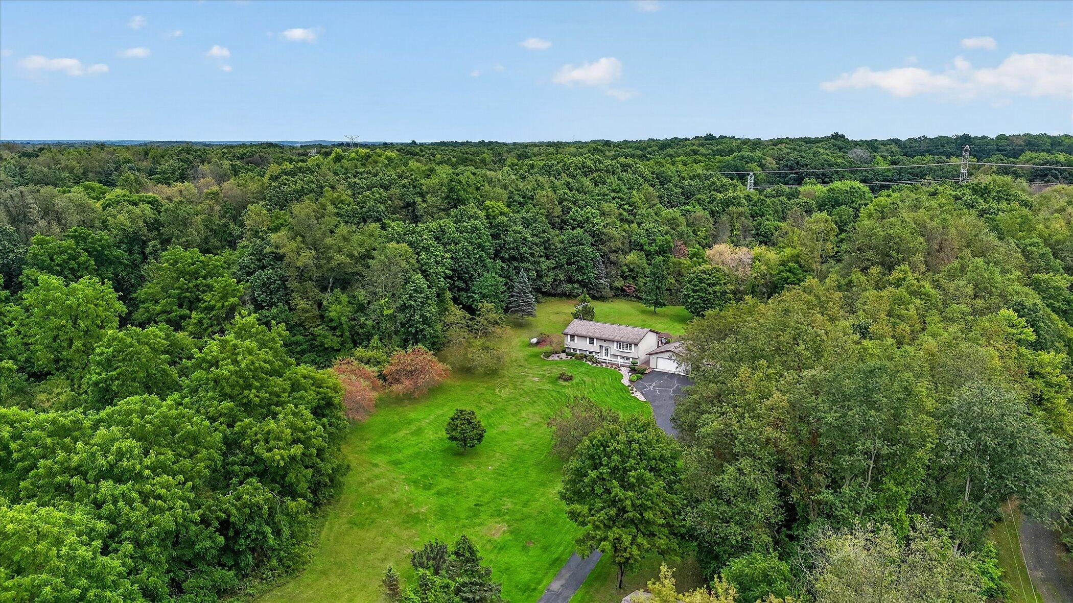 Aerial view of a house amid dense woods, with a broad lawn and long driveway.