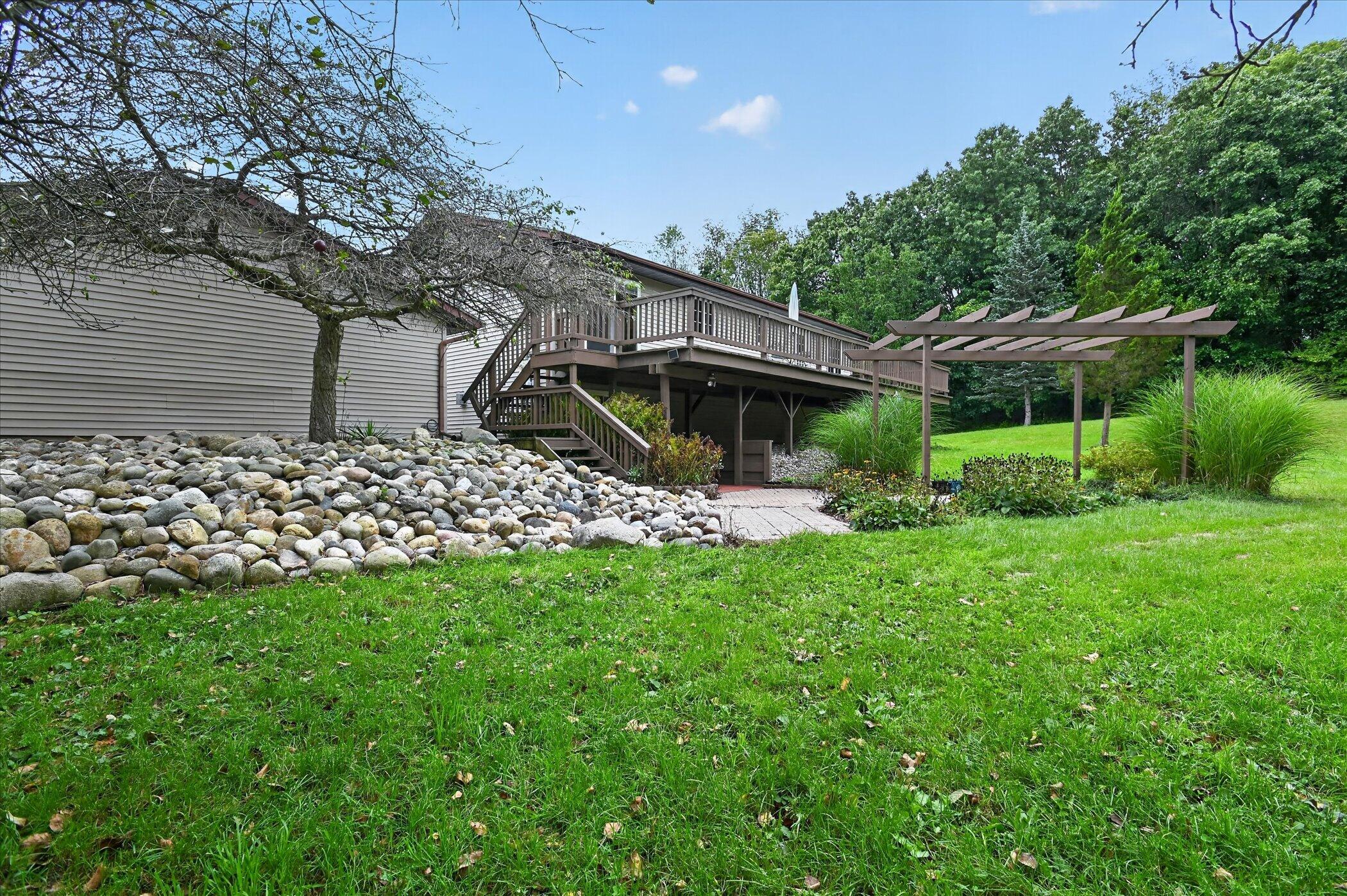 Home’s raised rear deck and pergola overlook a landscaped lawn and rock garden.