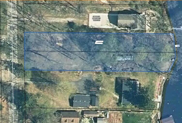 Aerial view of a wooded waterfront lot outlined by parcel boundaries beside neighboring properties.