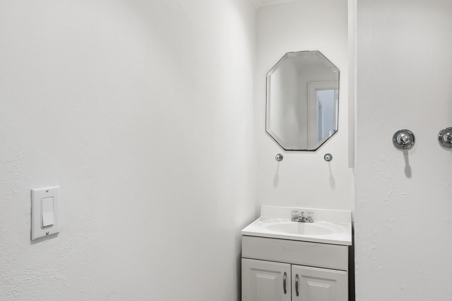 Bathroom vanity with a white sink, chrome fixtures, and an octagonal mirror.