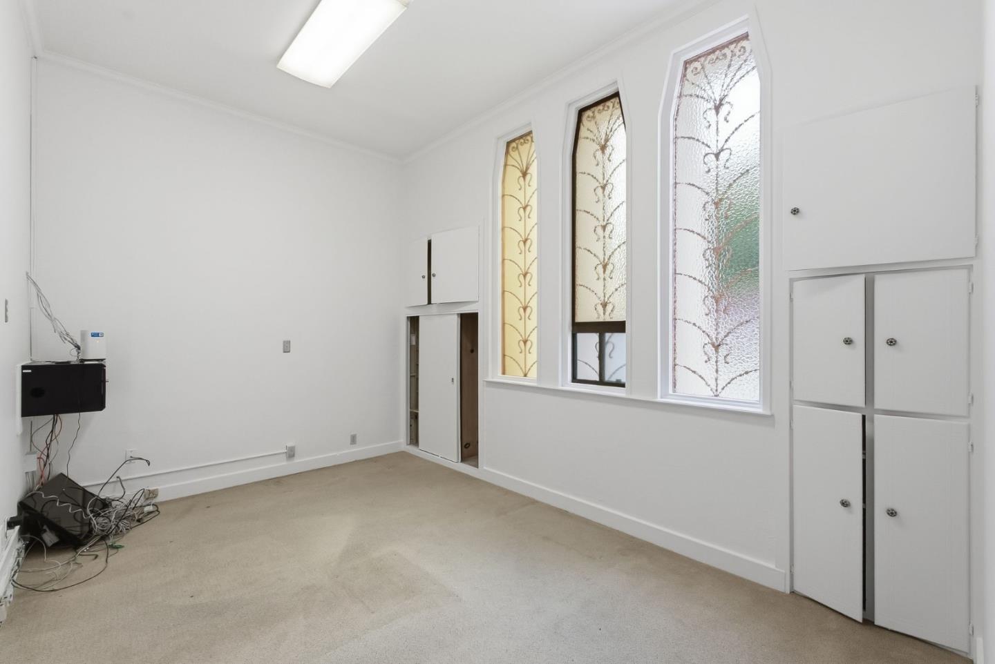 Empty carpeted room with tall decorative stained-glass windows and built-in storage cabinets.