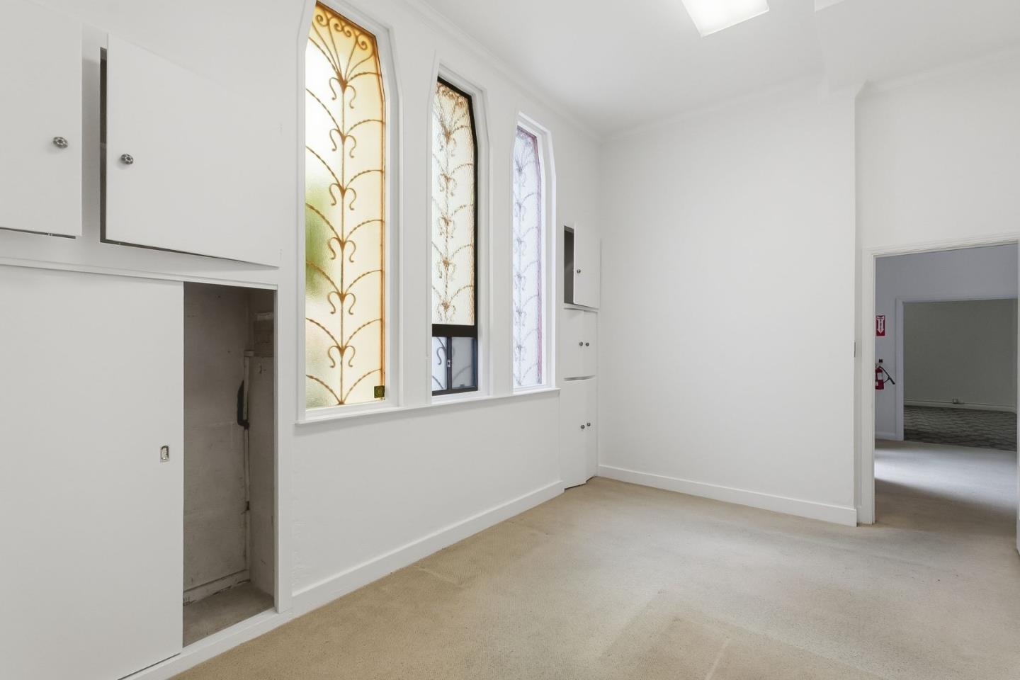 Vacant carpeted room with built-in white cabinets and three tall decorative leaded-glass windows.