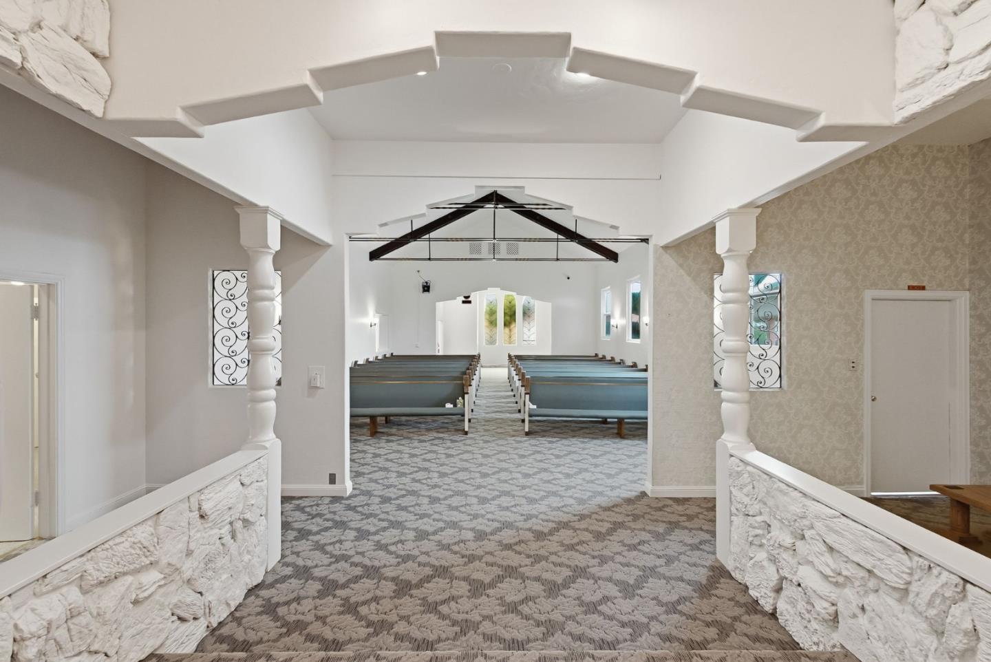 Church sanctuary with a carpeted aisle, rows of blue pews, and exposed roof trusses.