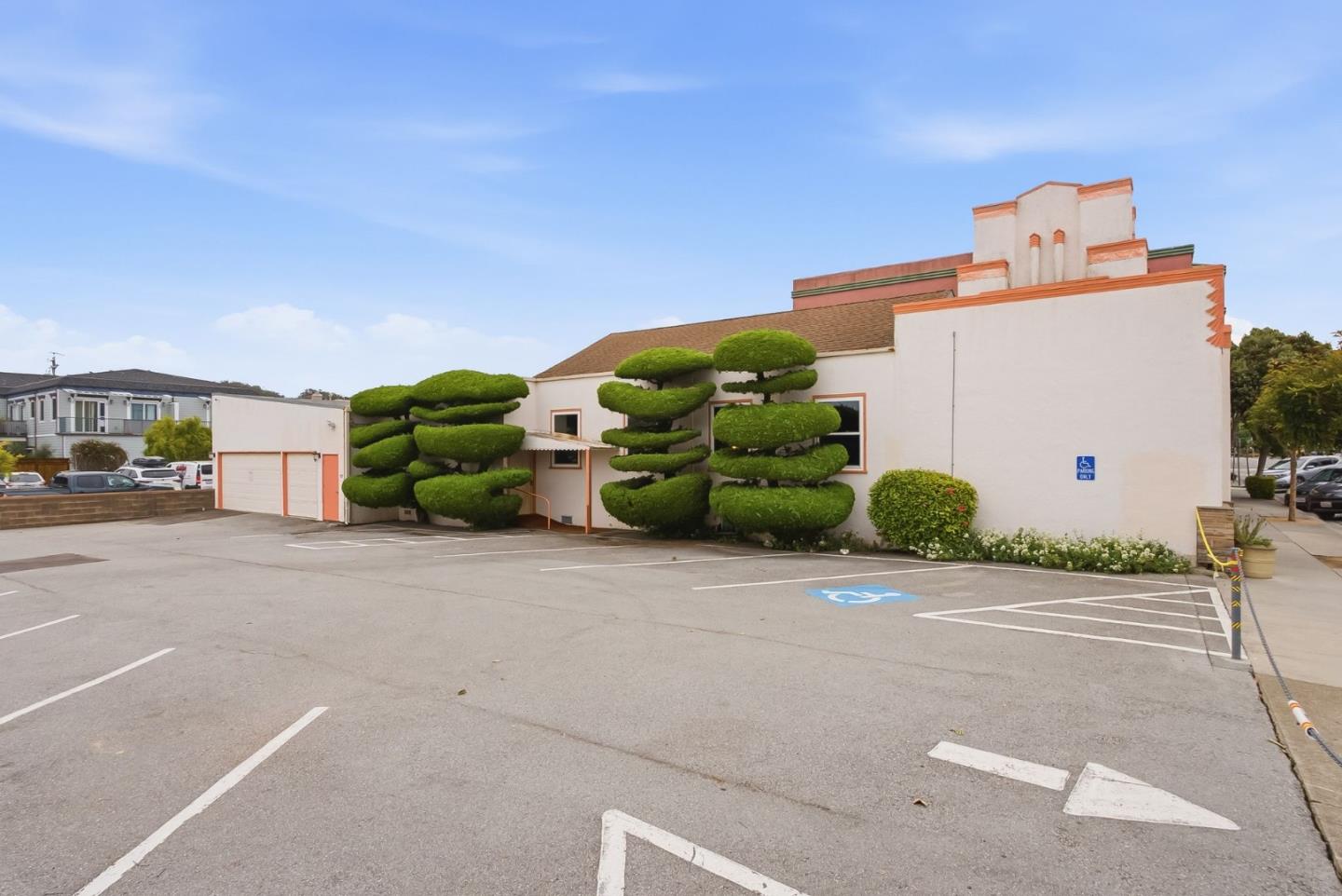Cream-colored building with terracotta trim, sculpted topiary, and a paved parking lot.