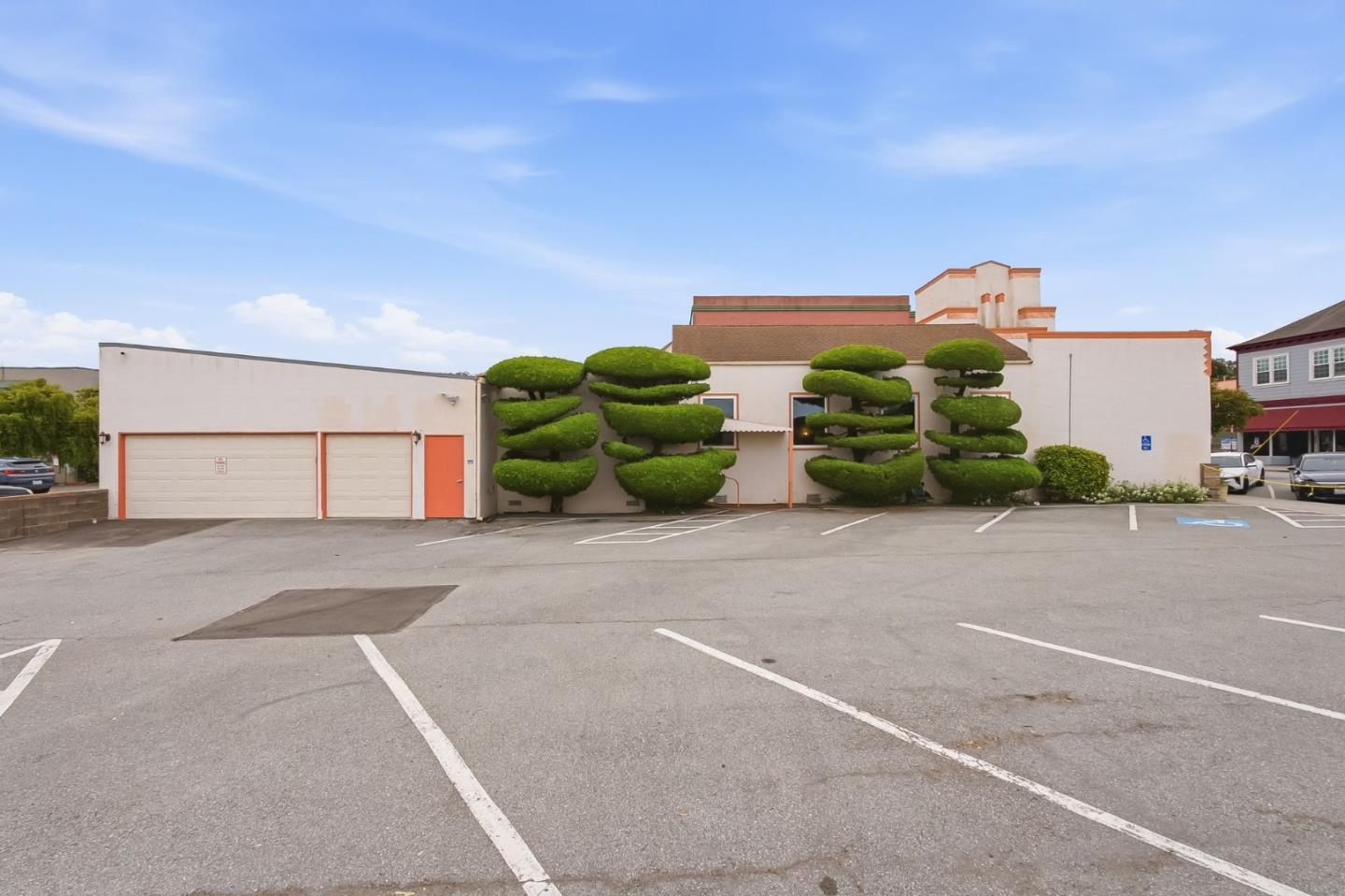 Low-rise building with sculpted topiary, garage doors, and a paved parking lot.