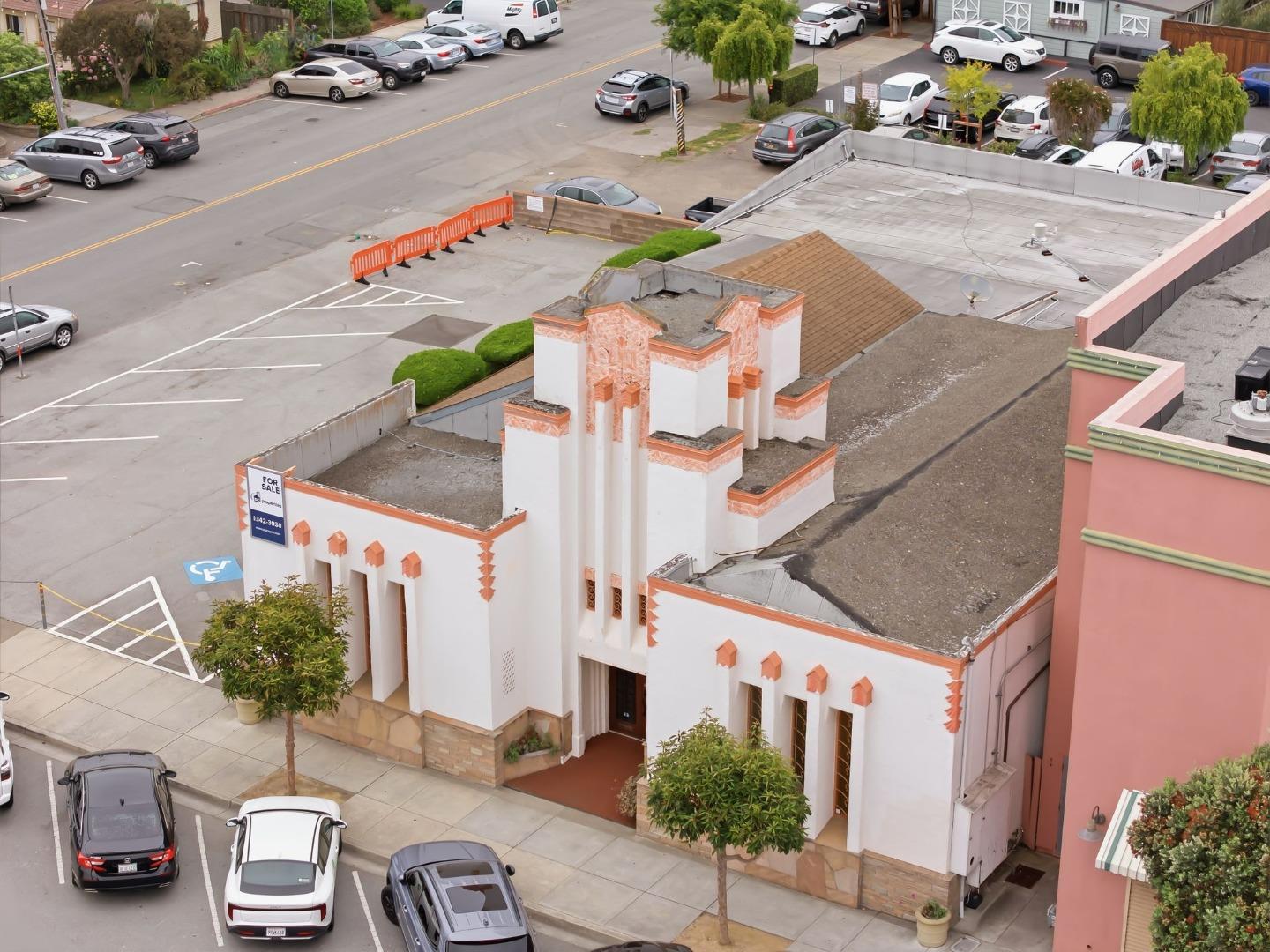 Commercial building with white stucco and orange trim, seen from above beside a street and parking lot.