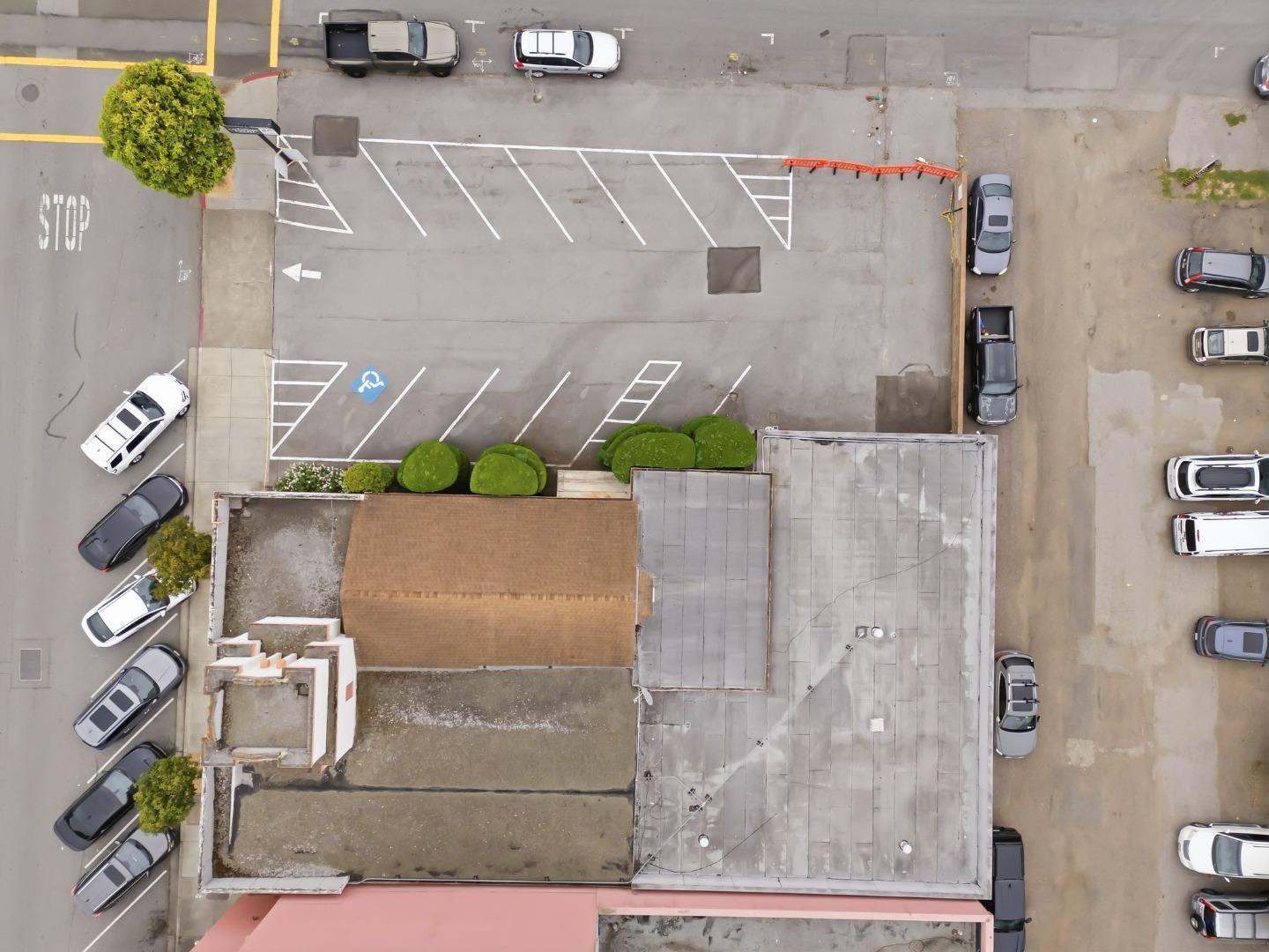 Aerial view of a low-rise building and surrounding parking lot with marked spaces and parked cars.