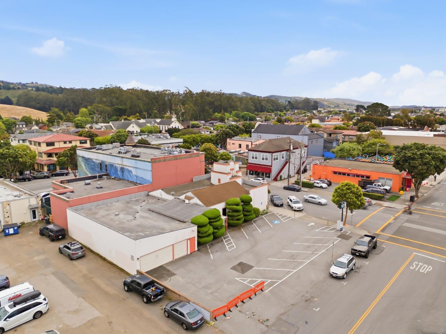 Aerial view of a low-rise downtown district, with colorful buildings and wooded hills beyond.