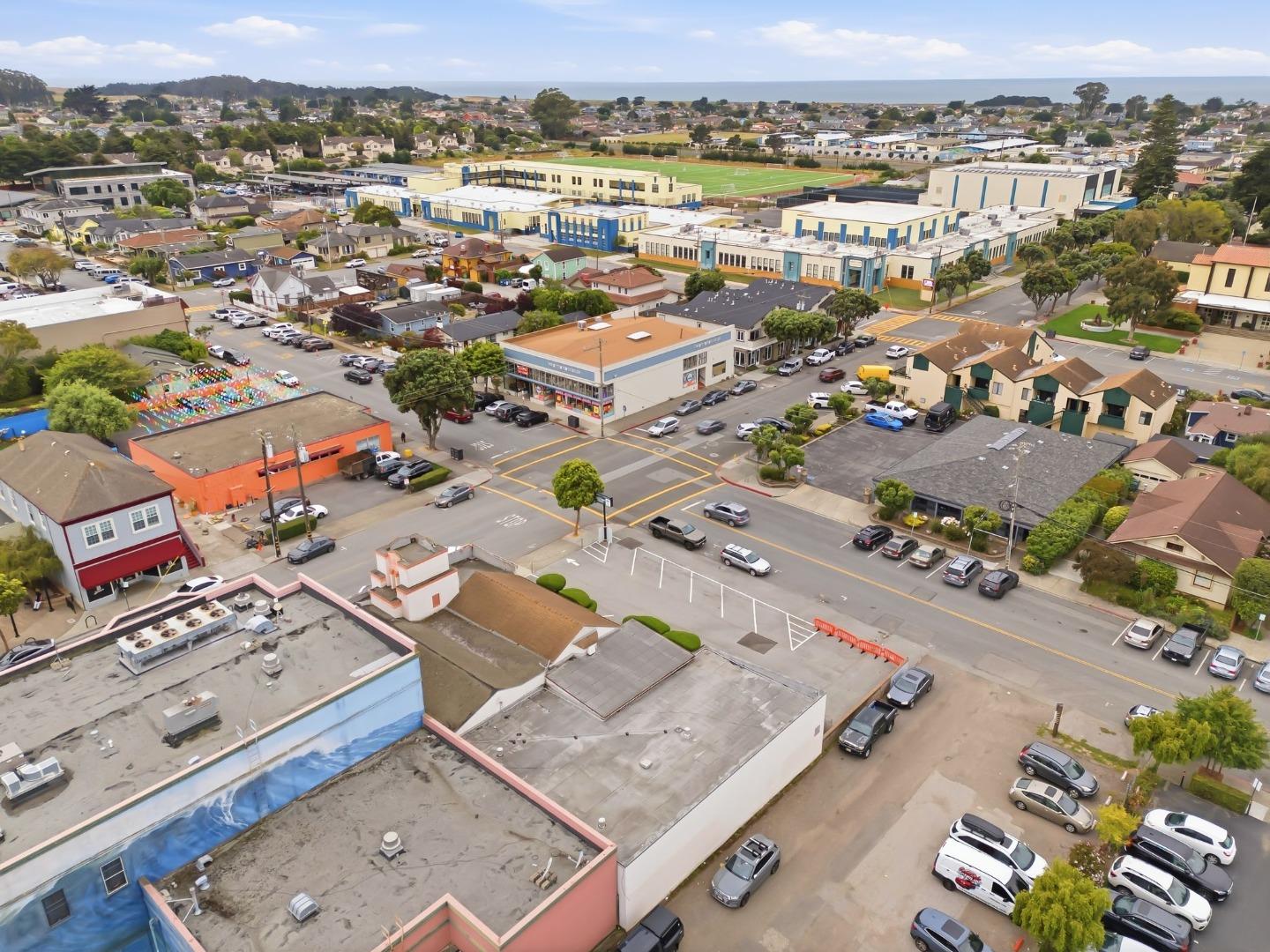 Aerial view of a coastal town, with a school campus and sports field near the ocean horizon.