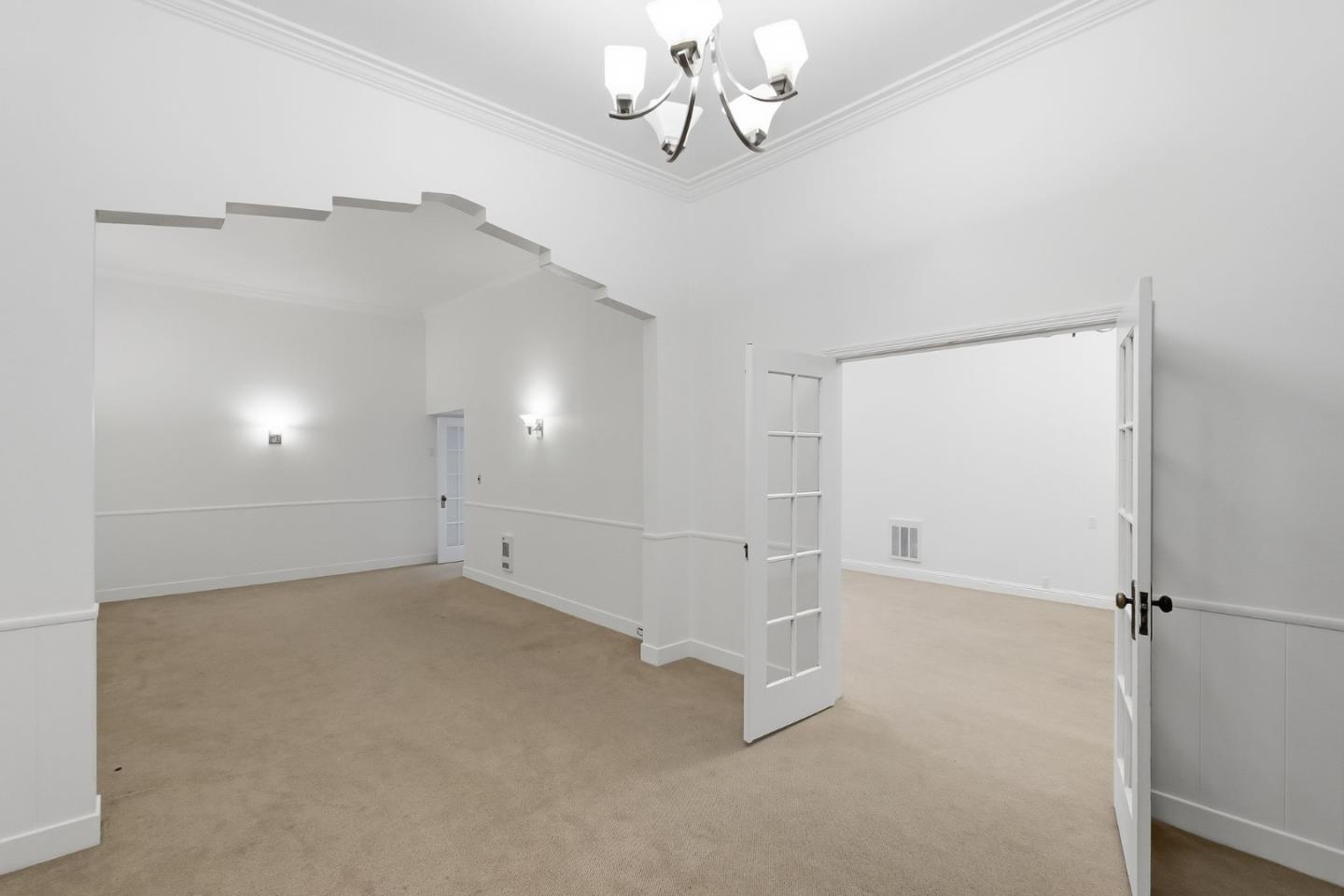Empty carpeted living room with a stepped archway and open French doors.