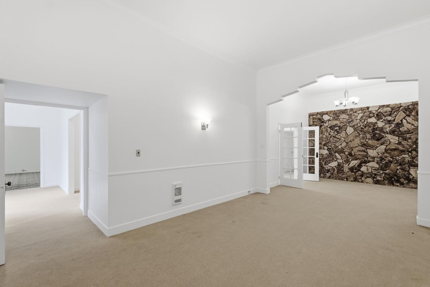 Vacant carpeted room with a stepped archway and a stone accent wall in the adjoining room.