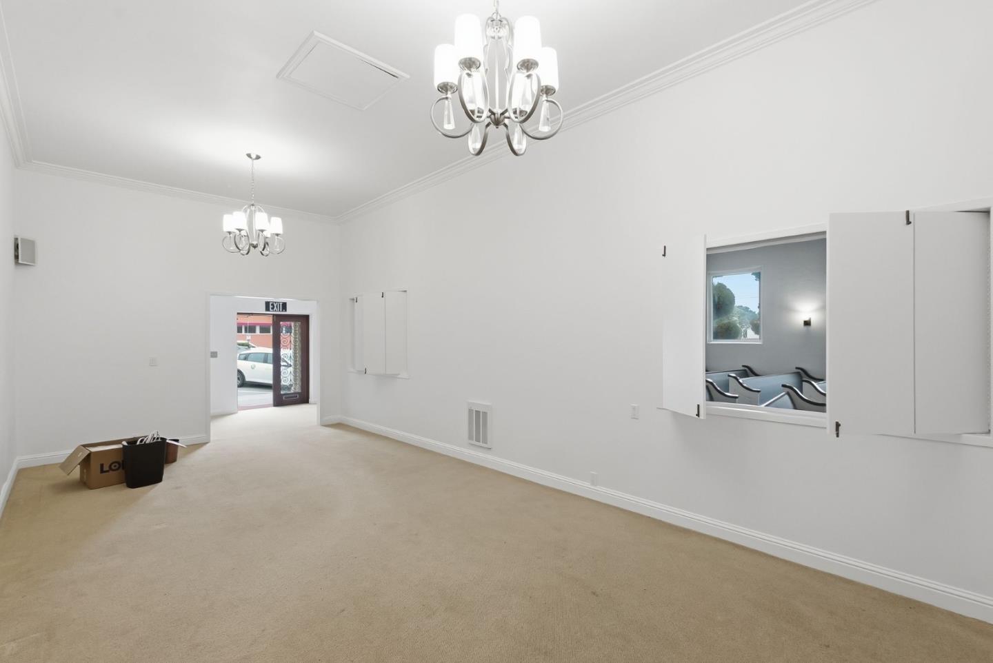 Vacant carpeted room with two chandeliers, an exit doorway, and a pass-through window.