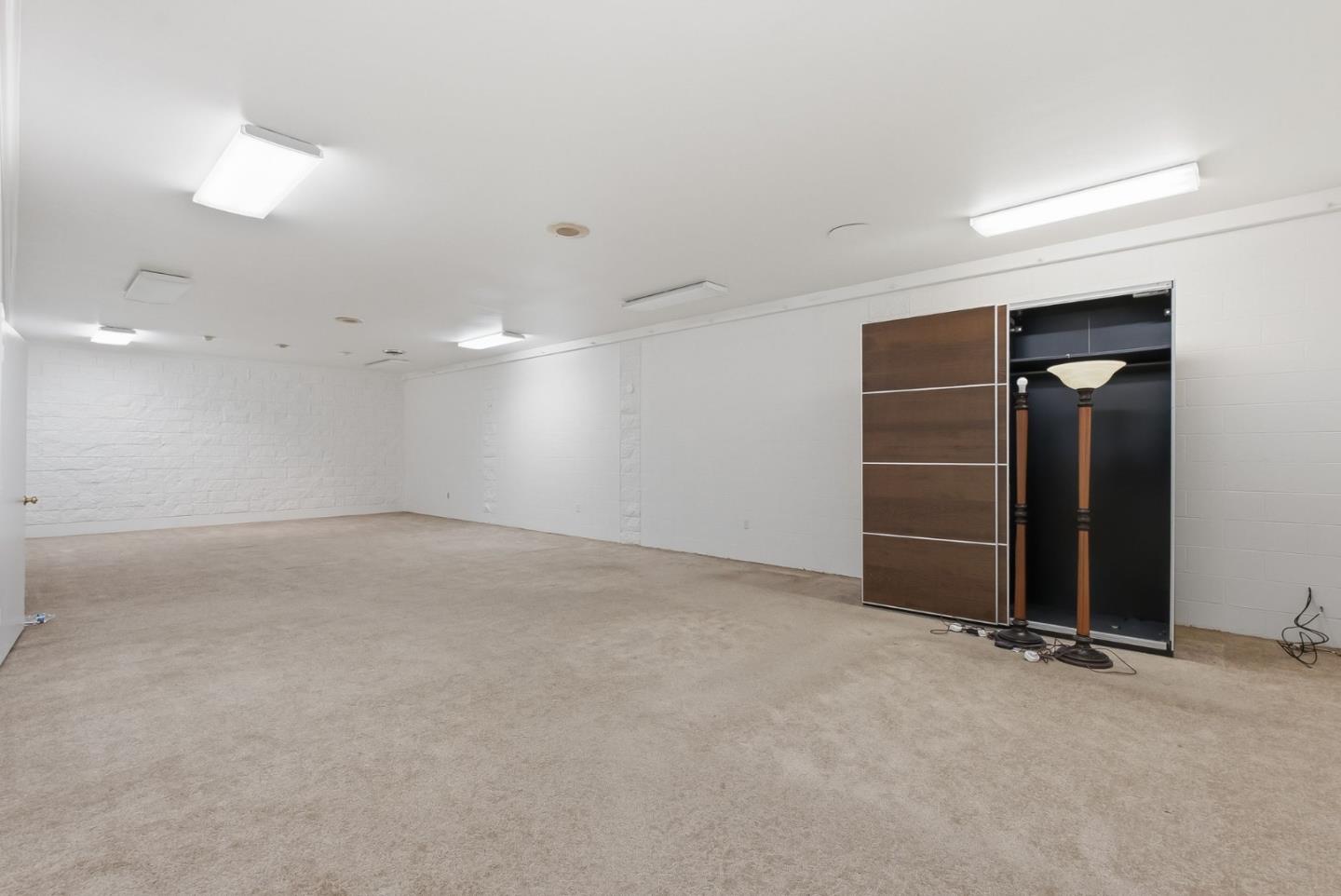 Empty carpeted room with white walls, ceiling lights, and an open cabinet holding two floor lamps.