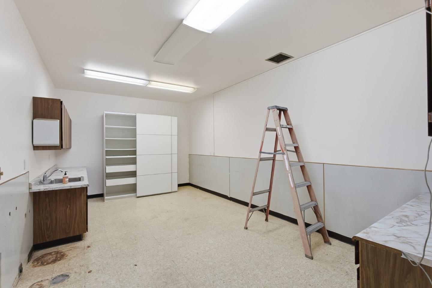 Bare utility room with a sink, open shelving, and a step ladder.