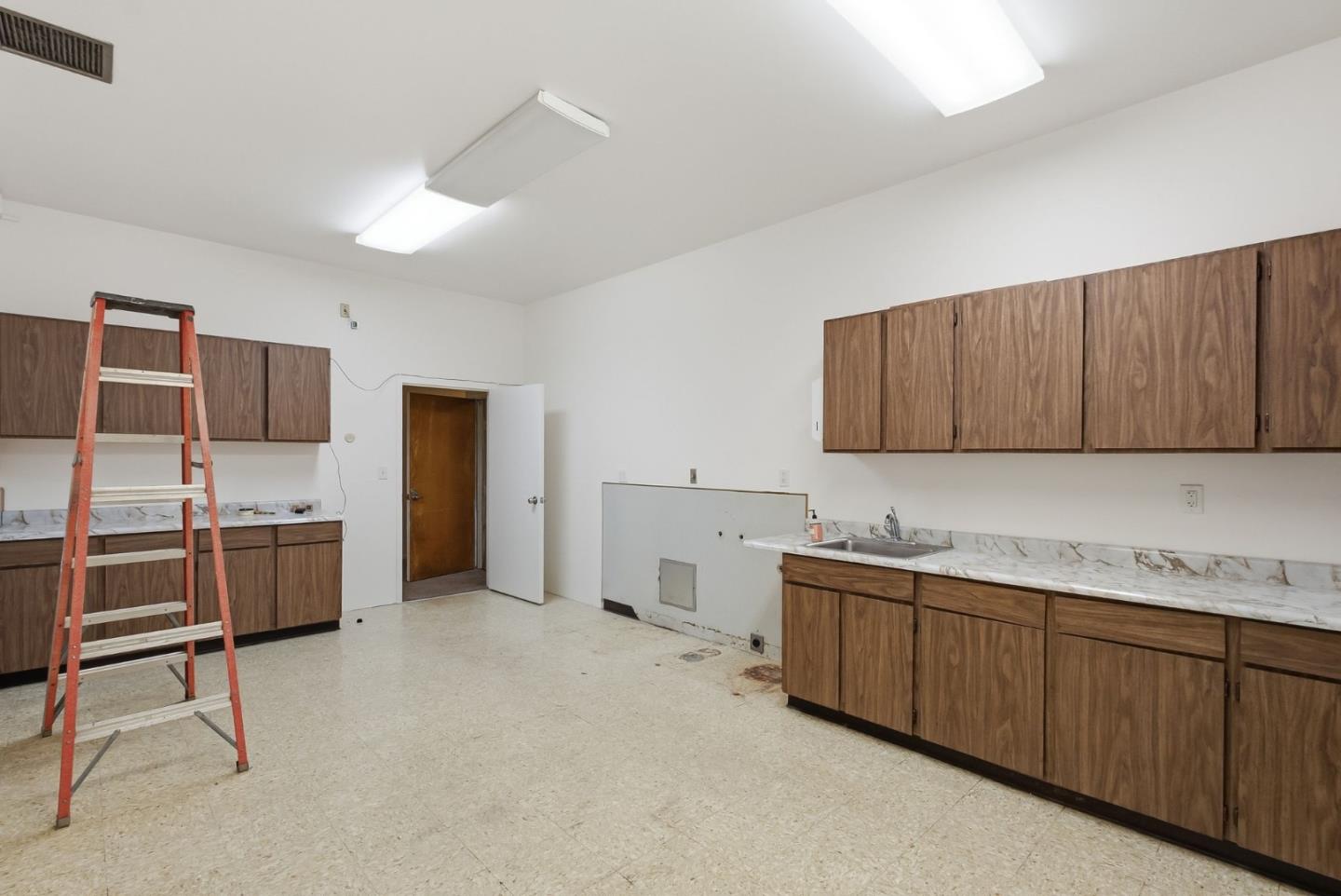 Vacant kitchen with brown cabinets, marble-pattern counters, a sink, and a red step ladder.