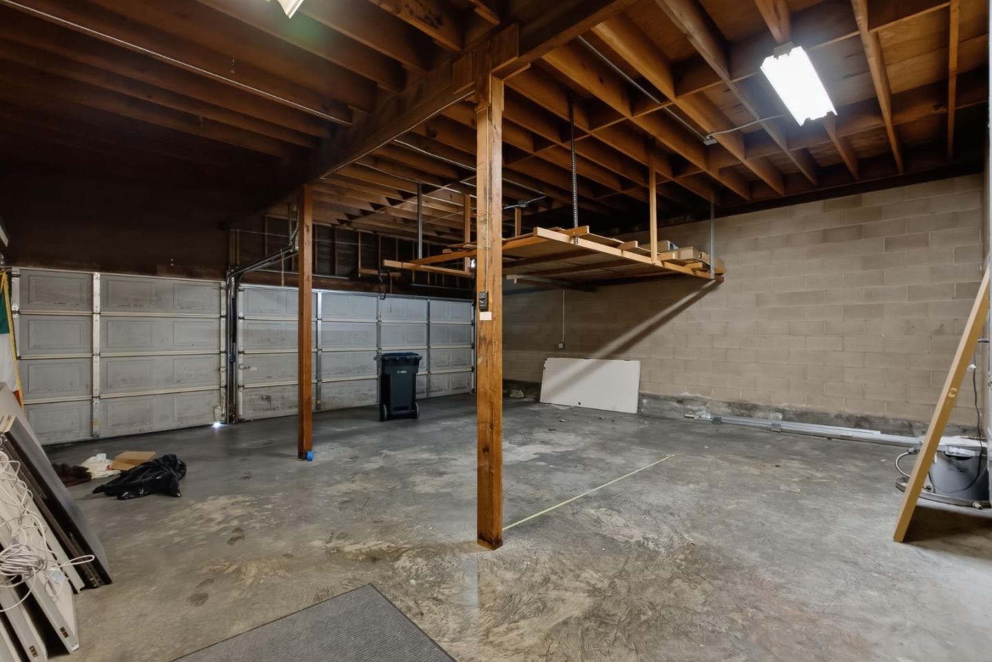 Spacious unfinished garage with exposed roof framing, multiple garage doors, and an elevated wooden storage platform.