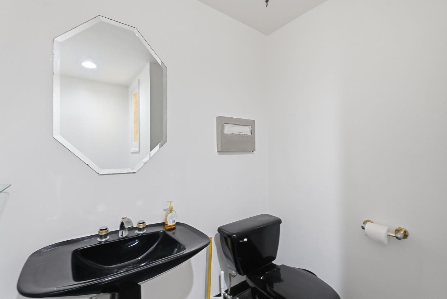 Bathroom with a black sink and toilet beneath a large octagonal mirror.