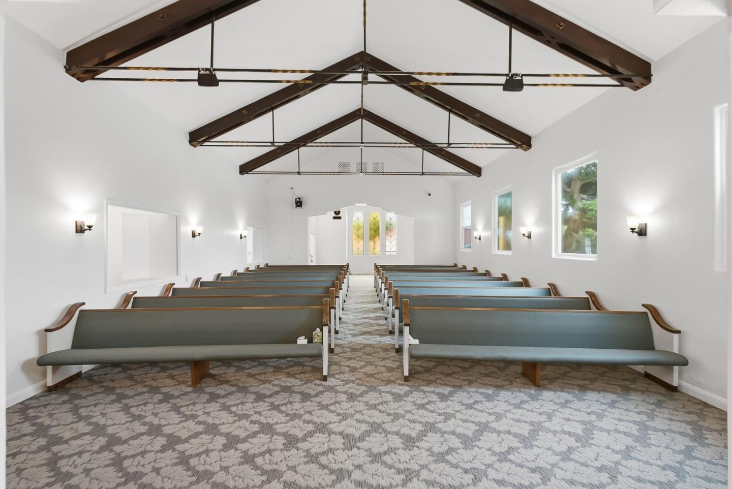 Chapel interior with rows of green pews, stained-glass windows, and exposed ceiling beams