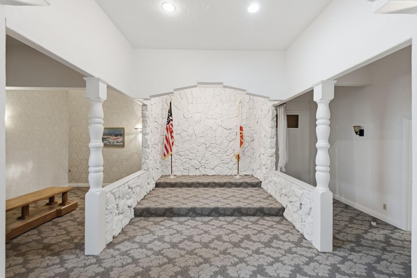 Foyer with a raised carpeted platform, white stone walls, and two flags.