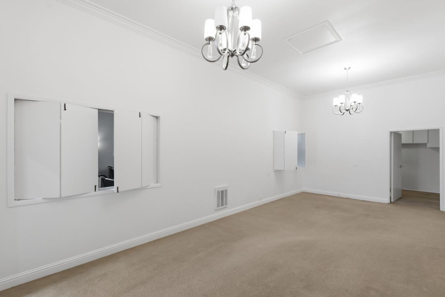 Empty carpeted room with two chandeliers and a shuttered pass-through window.