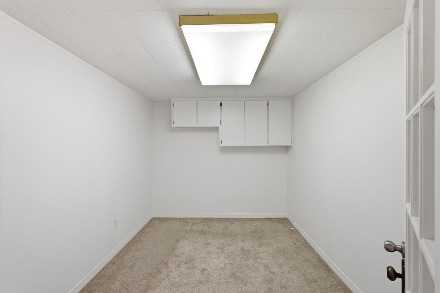 Empty carpeted room with white walls, high cabinets, and a bright ceiling light.