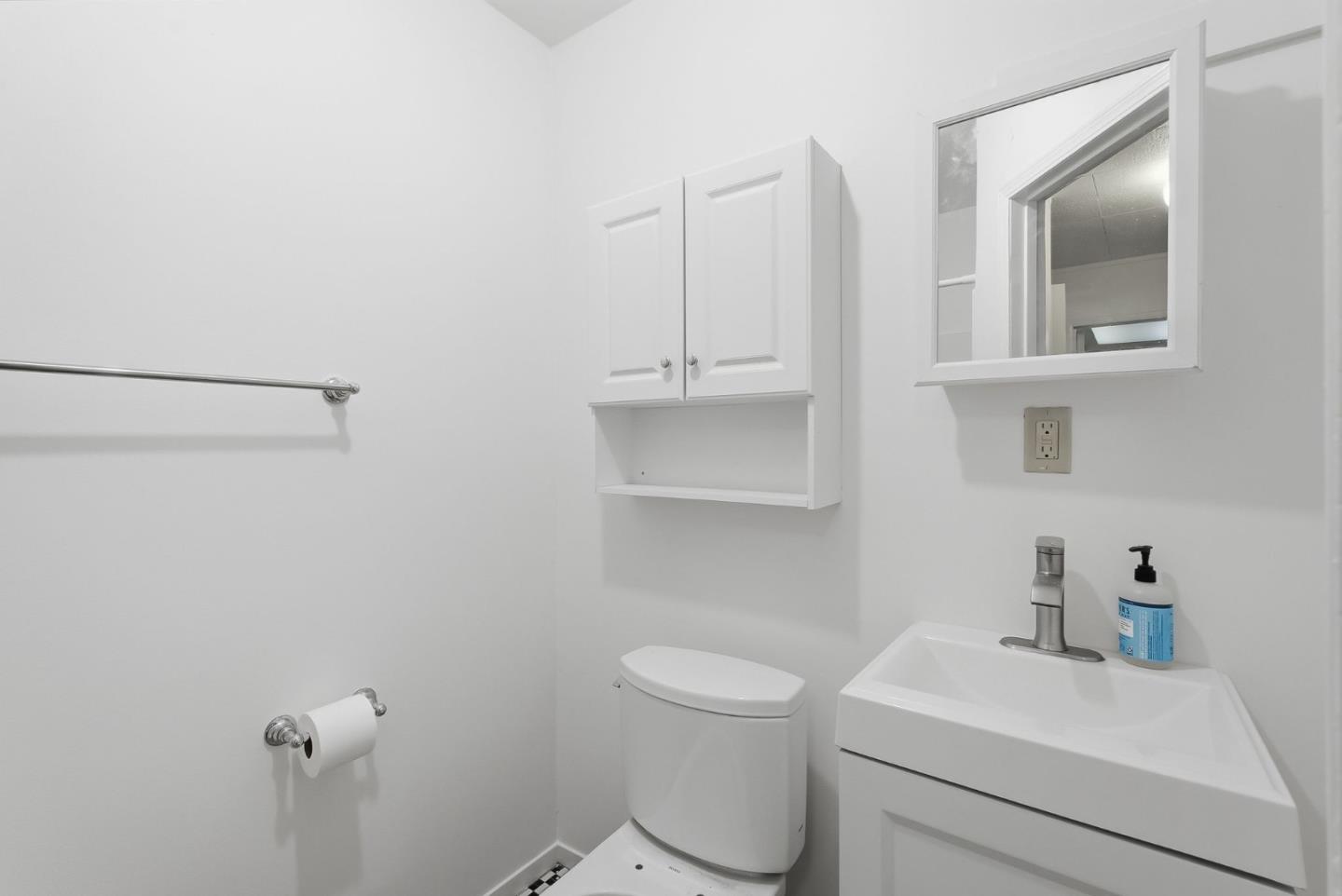 Compact white bathroom with a toilet, sink vanity, wall cabinet, and grab bar.