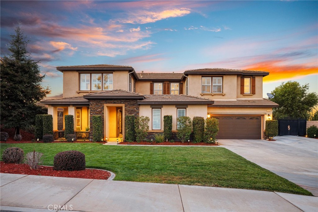 Two-story stucco home with stone-accented entry, landscaped lawn, and attached two-car garage at sunset.