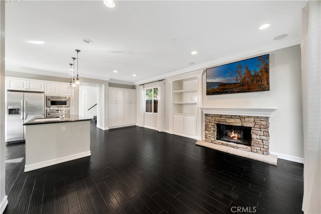 Open-plan living room and kitchen with a stone fireplace, white cabinetry, and dark wood floors.