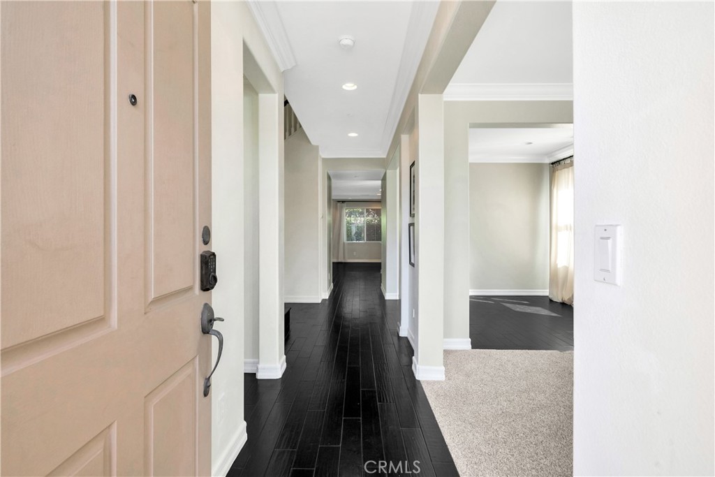 Entryway with dark plank hallway flooring and an adjoining empty carpeted room.