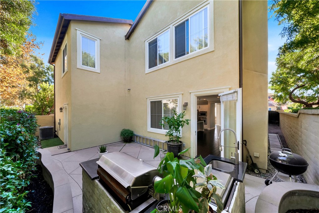 Rear patio with an outdoor kitchen and grill beside the home’s open doorway.