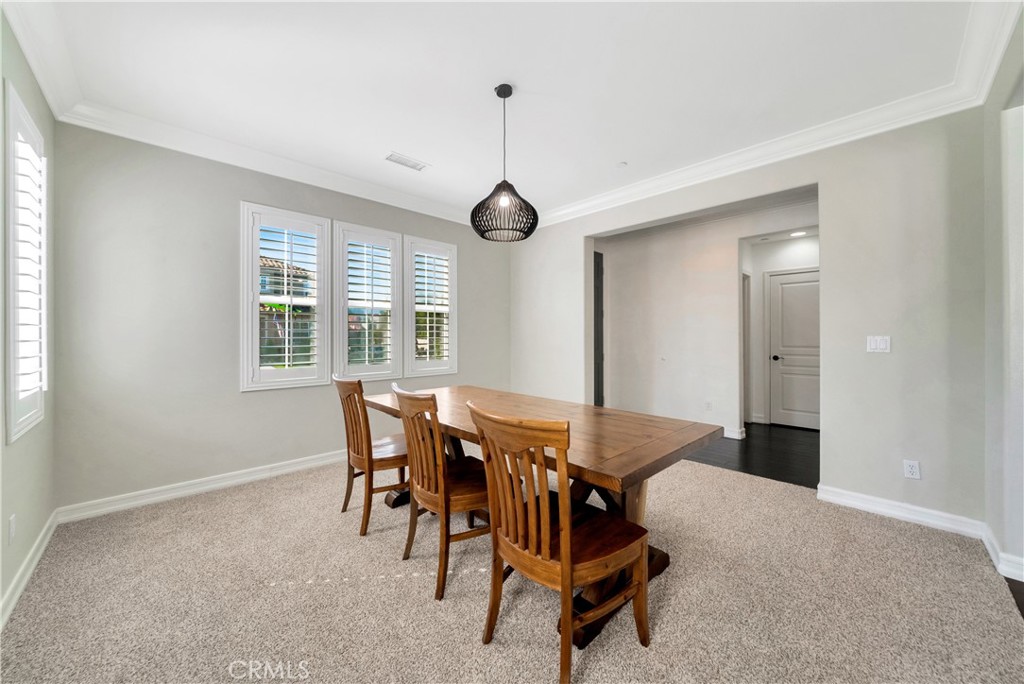 Dining room with a wooden table, matching chairs, shuttered windows, and a dark pendant light.