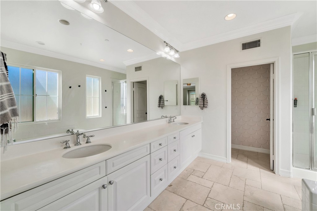 Bathroom with a long white double vanity, broad mirror, pale stone tile floor, and glass shower.