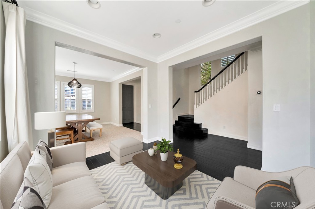 Staged living room with cream sofas and geometric rug, open to dining area and staircase.