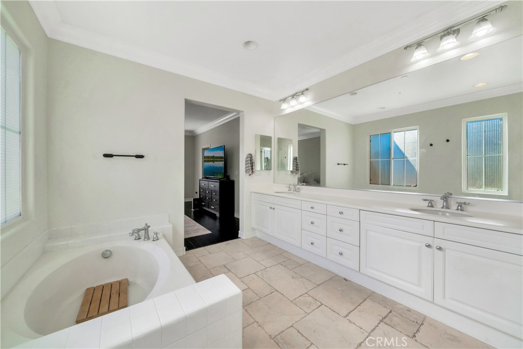 Bathroom with a soaking tub, long double vanity, large mirror, and stone tile flooring.