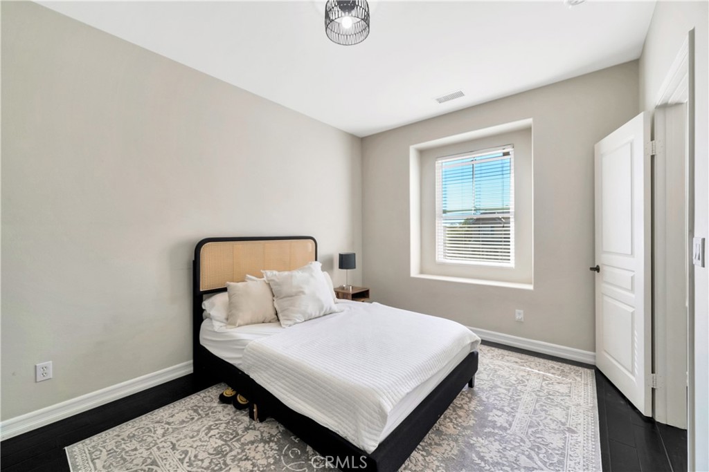 Bedroom with a cane-panel headboard, white bedding, patterned rug, and a window with blinds.