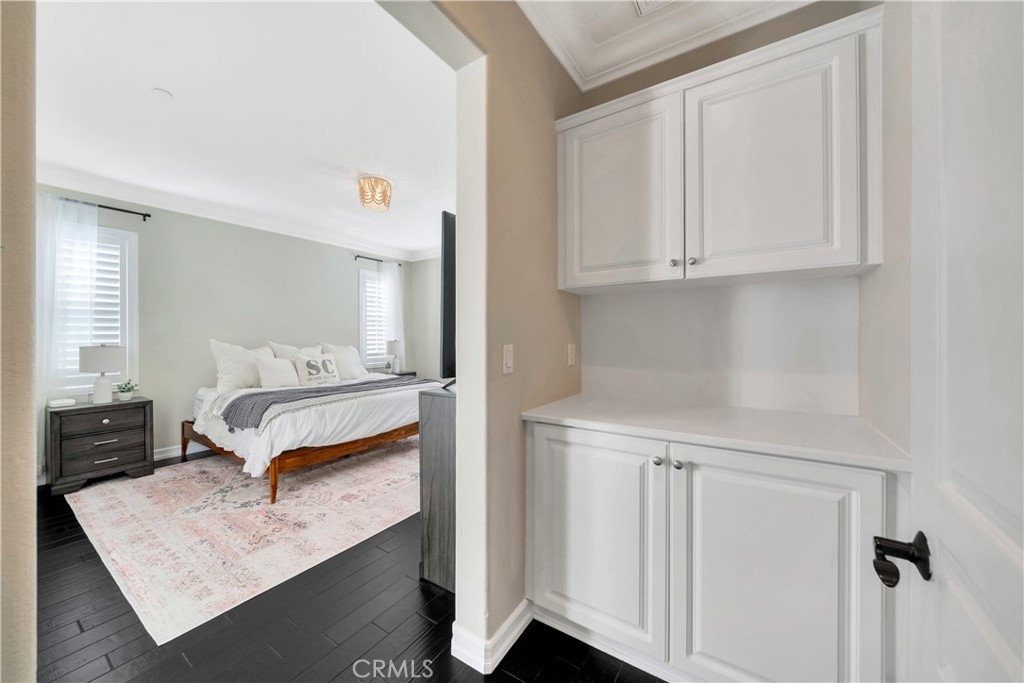 Staged bedroom with white built-in cabinets, a white bed, shuttered windows, and dark wood flooring.