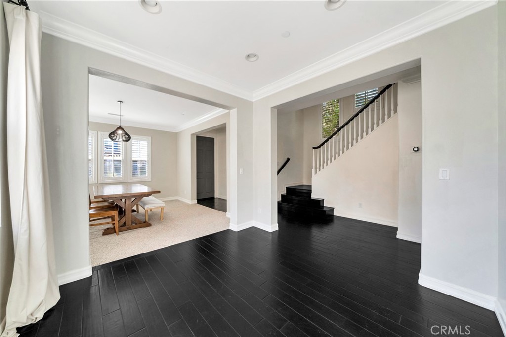 Foyer with dark flooring, staircase, and adjoining dining area with a wooden table.