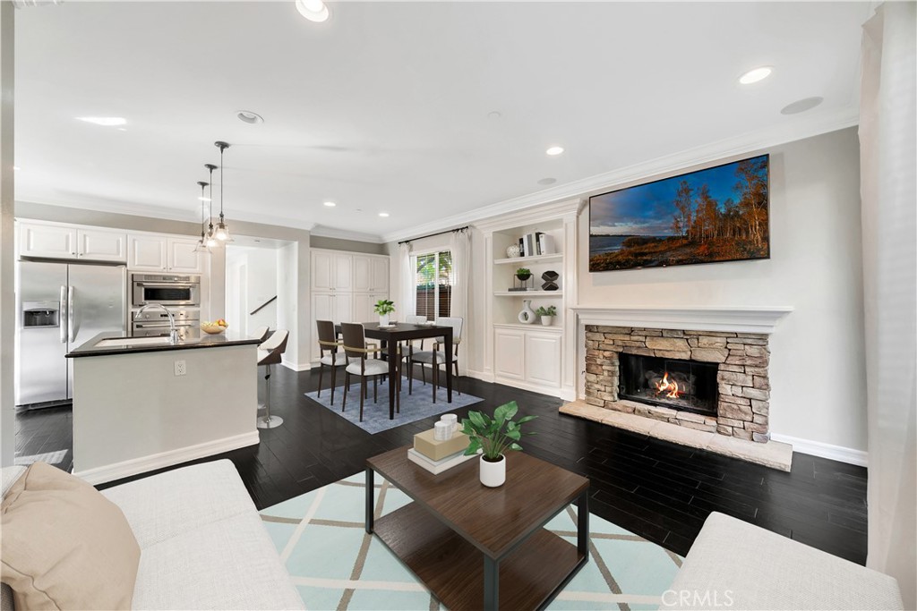 Open-plan living room with a stone fireplace, dark floors, and adjoining white kitchen.