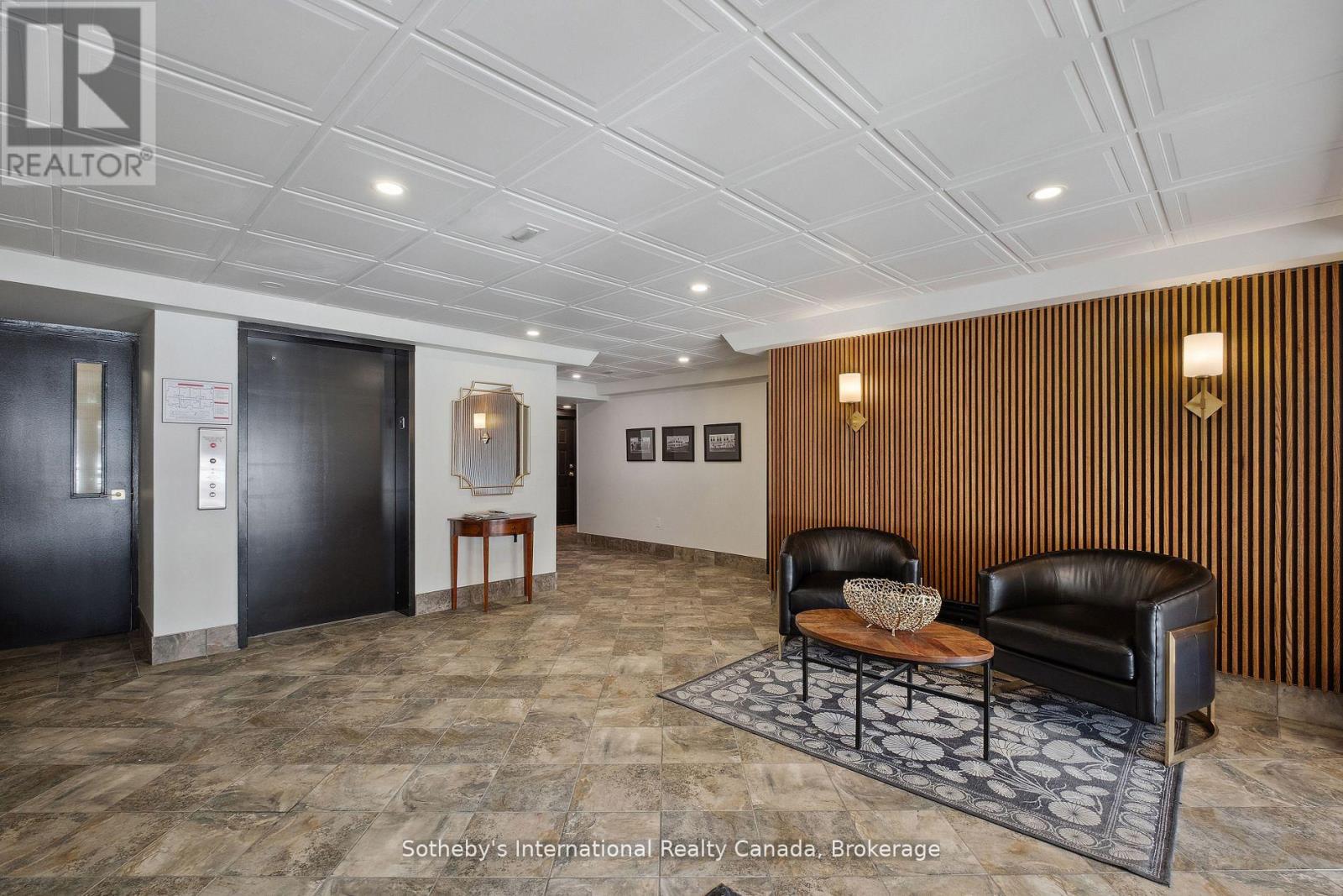 Building lobby with black elevator doors, leather seating, and a wood-slat accent wall.