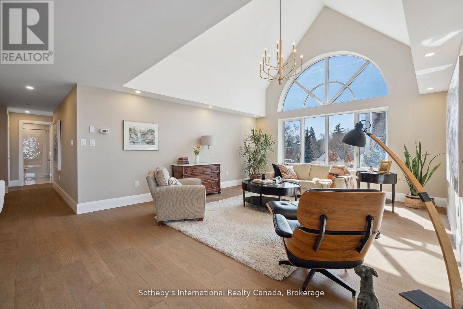 Furnished living room with a vaulted ceiling, arched window, and wood flooring.