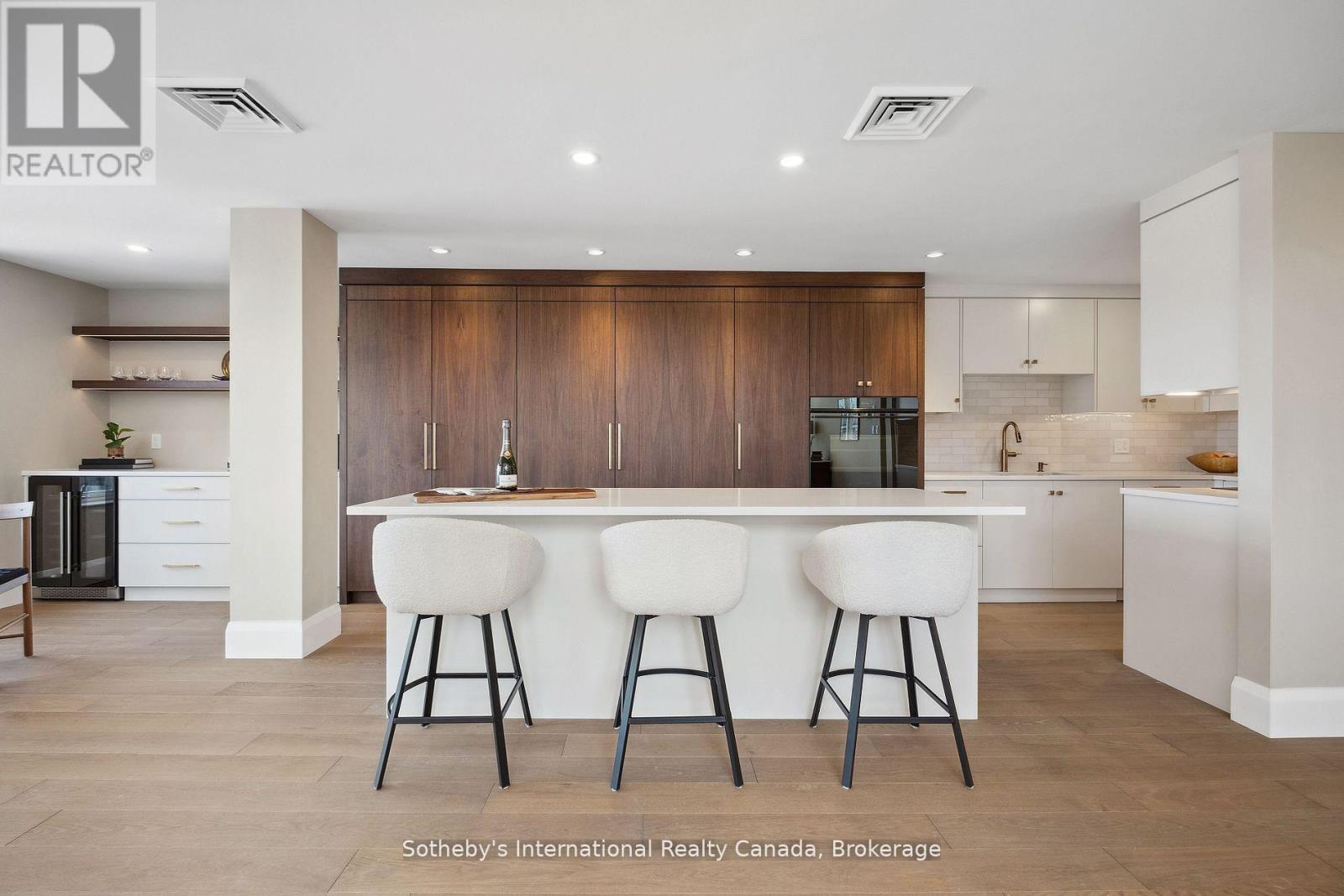 Modern kitchen with a white island, three bar stools, and dark wood cabinetry.