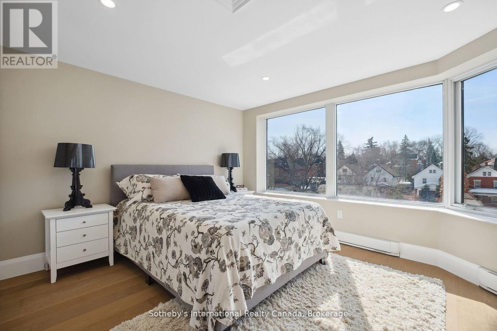 Bedroom with floral bedding, hardwood floors, and large windows overlooking the neighborhood.
