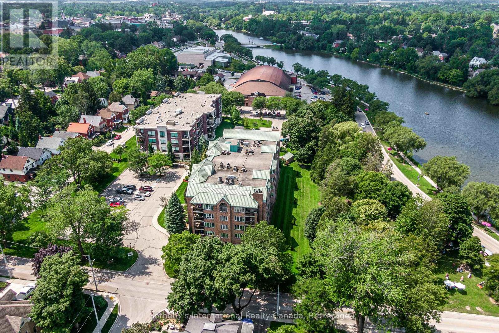 Aerial view of a brick condominium beside a river, with landscaped grounds and a waterfront path.