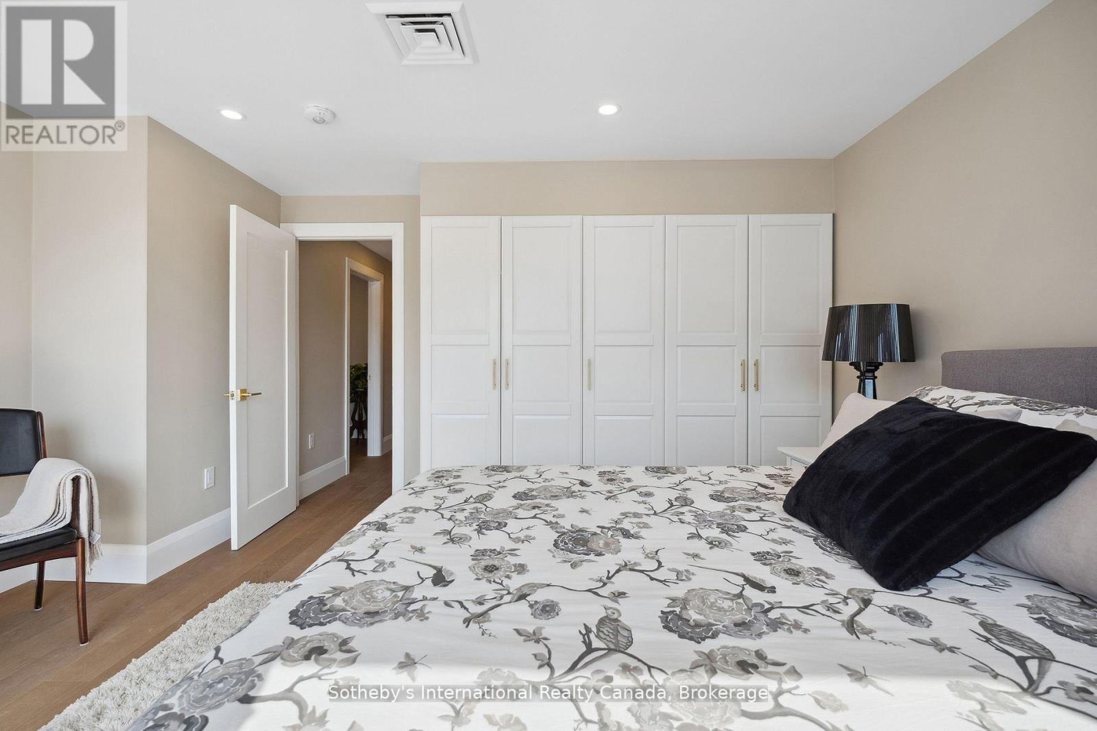 Bedroom with gray floral bedding, white built-in wardrobes, and hardwood flooring.